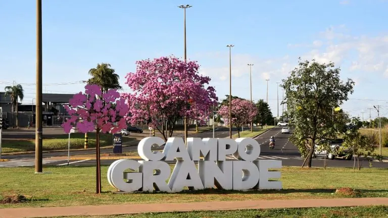 Letreiro de Campo Grande com ipês floridos representando expansão urbana
